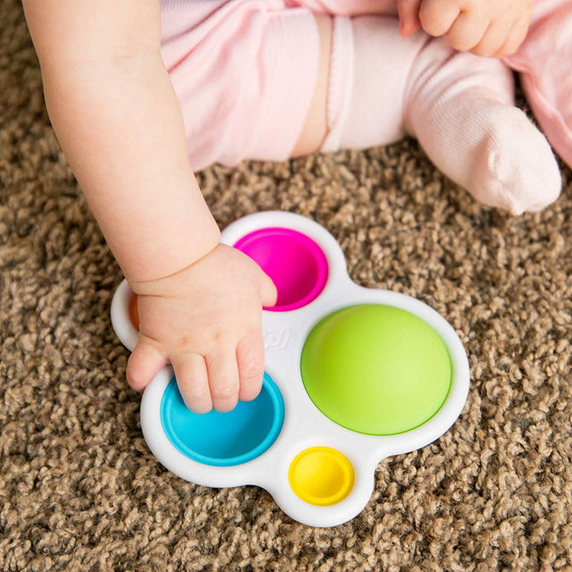 Baby's hand pressing colorful silicone bubbles on white ABS plastic frame of Dimpl sensory toy.