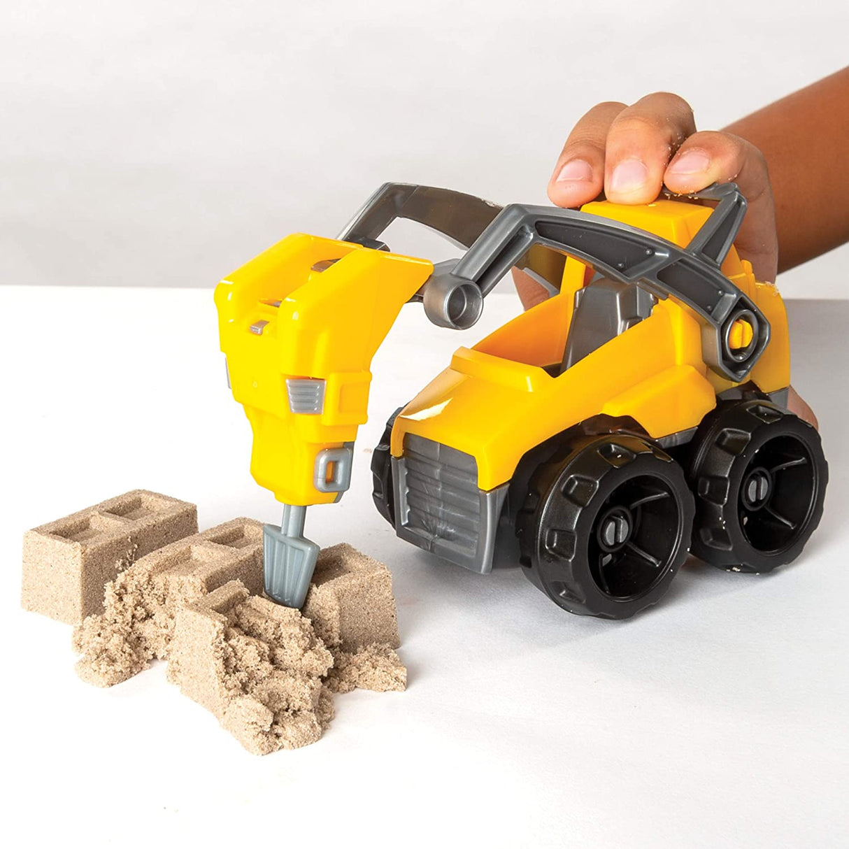 Child playing with the Kinetic Sand Dig & Demolish set using the truck and jackhammer to crush molded sand bricks.