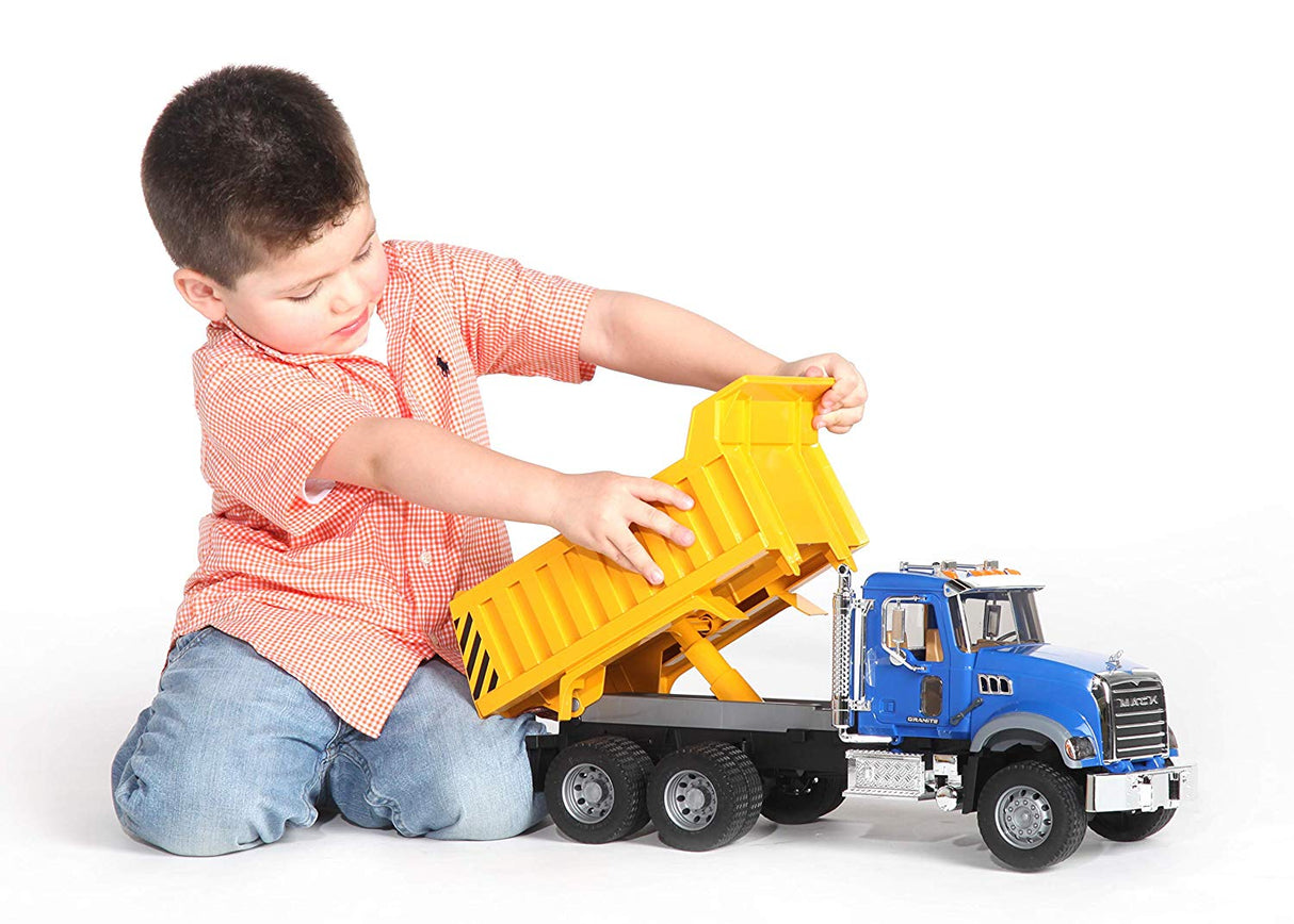 Child playing with Mack Granite Tip Up Truck toy featuring a tilting yellow dump bed and detailed blue cabin.
