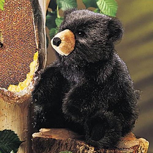 Baby Black Bear Puppet with soft black fur and sweet face sitting on a log near a tree hollow.