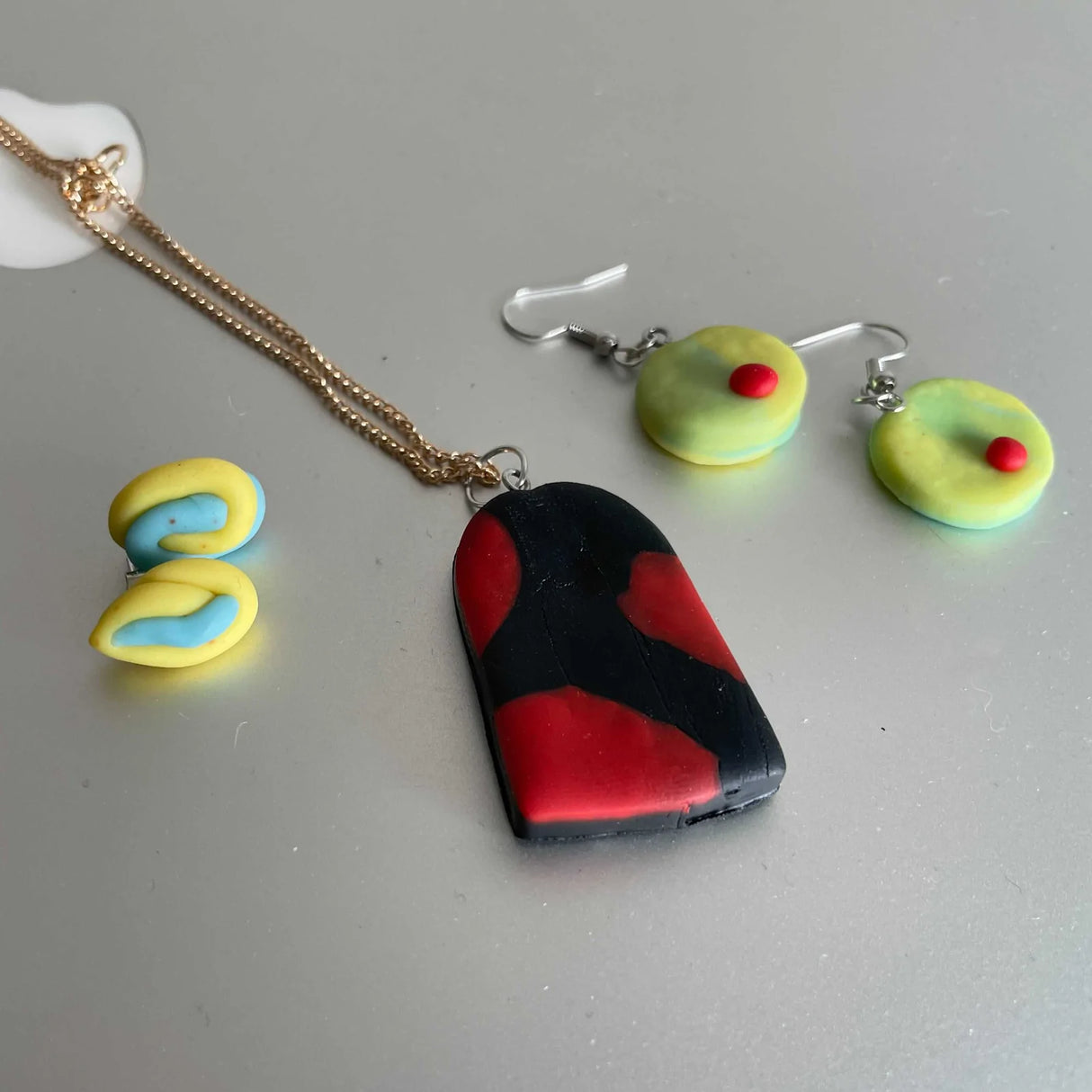 Crafters Polymer Clay Jewelry featuring handmade colorful clay earrings and a bold red and black pendant necklace.