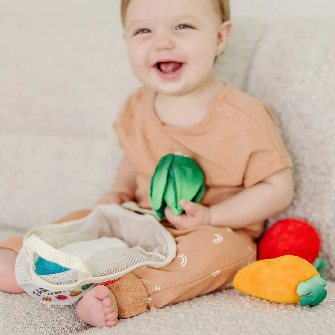 Baby playing with Fill & Spill Market Basket featuring plush veggies like carrot, lettuce, and tomato with mesh tote.