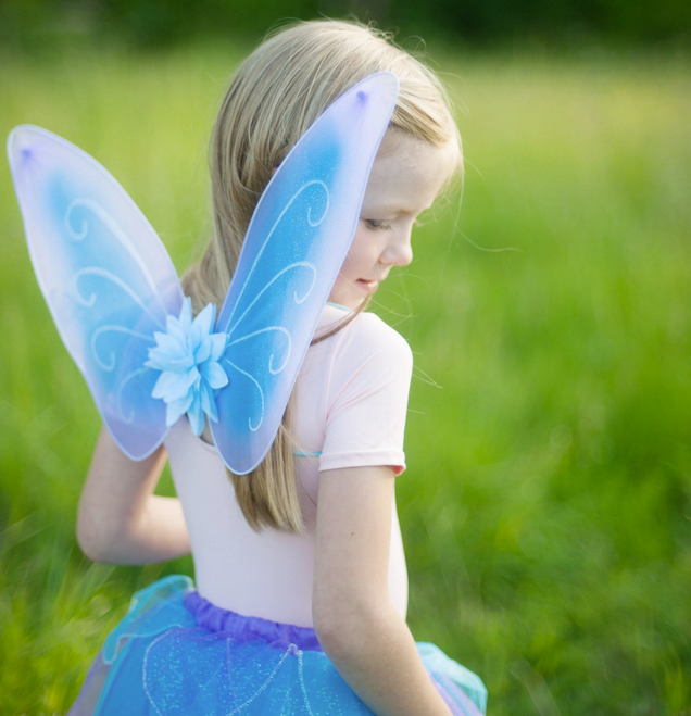 Child wearing the Fancy Flutter Skirt Set | Blue with glitter wings and a matching blue skirt outdoors.