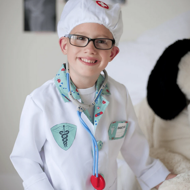 Child dressed in Doctor Set costume with white coat, stethoscope, and hat, smiling and playing pretend doctor.
