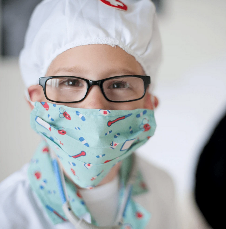 Child wearing the Doctor Set costume with white hat, patterned fabric mask, and black glasses.