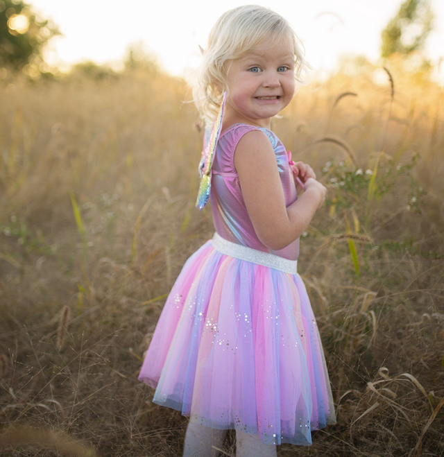 Young girl smiling outdoors wearing Rainbow Sequin Skirt, Wings & Wand set with pastel tulle skirt and sparkly wings.