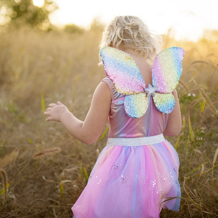 Child wearing Rainbow Sequin Skirt, Wings & Wand with pastel tutu skirt and rainbow sequin wings outdoors in sunlight.