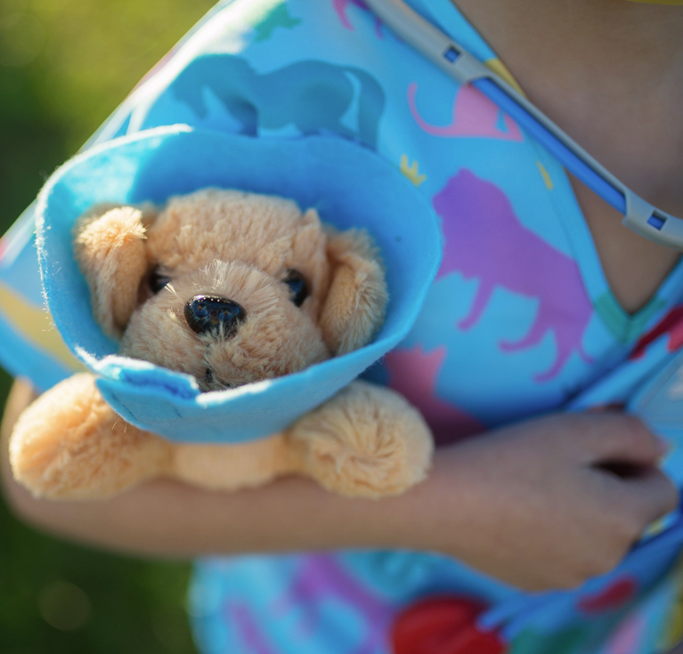 Child holding plush puppy wearing cone in colorful scrubs from the Veterinarian Set for imaginative play.