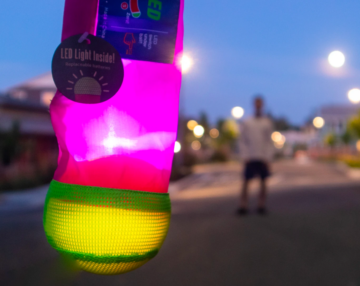 Foxtail LED Softie glowing brightly at dusk, featuring a colorful mesh foam ball with a long nylon tail.