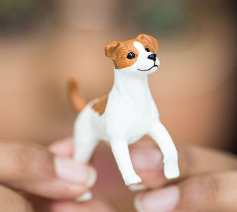 Close-up of a hand holding a detailed Jack Russell Terrier figurine with white and brown markings.