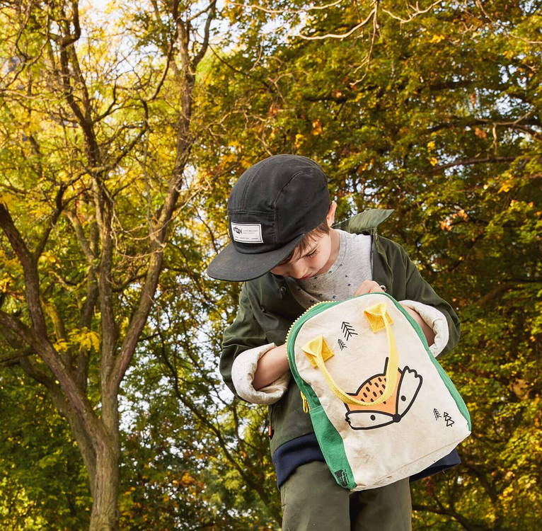 Child outdoors holding a green and cream Zipper Lunch Bag | Fox with a fox design and yellow zipper pull.