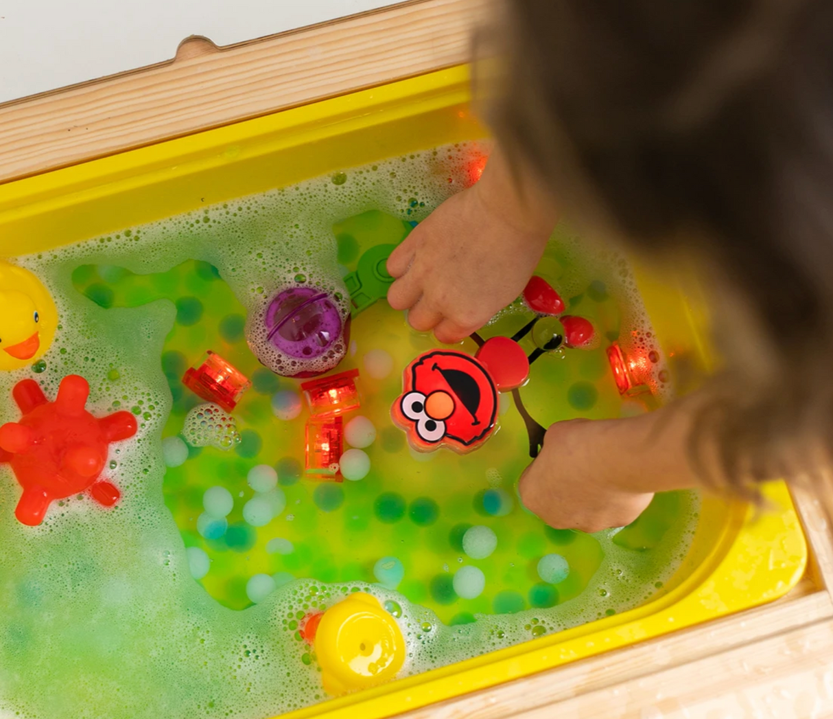 Child playing with Glo Pals Elmo Character in a bubbly water play tray with light-up cubes.