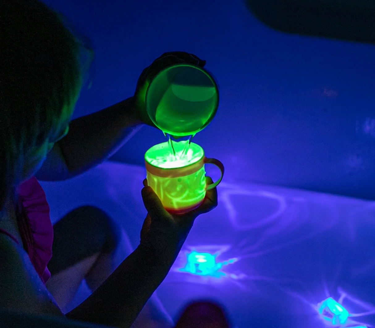 Child pouring glowing green liquid into a cup in a dark room featuring Glo Pals Green light-up cubes.