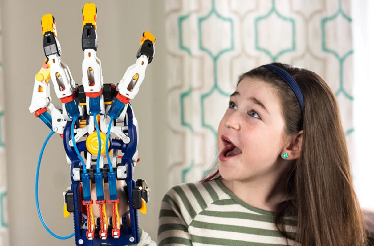 A girl excitedly operates the colorful Mega Cyborg Hand, a hydraulic mechanical glove simulating real finger movements.