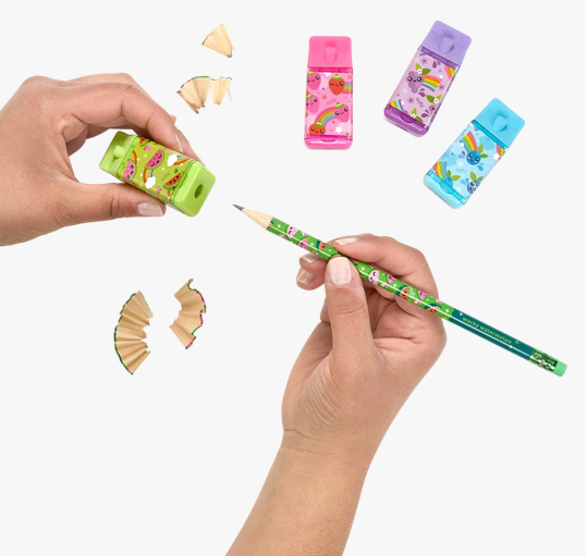 Hands sharpening a pencil with a green Lil Juicy Box Eraser & Sharpener and colorful sharpeners nearby