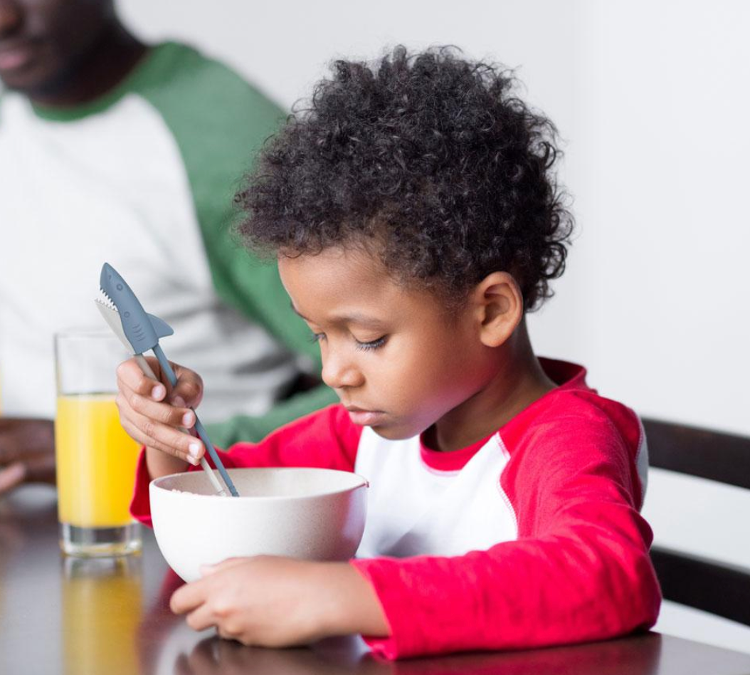 Young child using Munchtime Chopsticks Shark with biting action to eat from a bowl at the table.