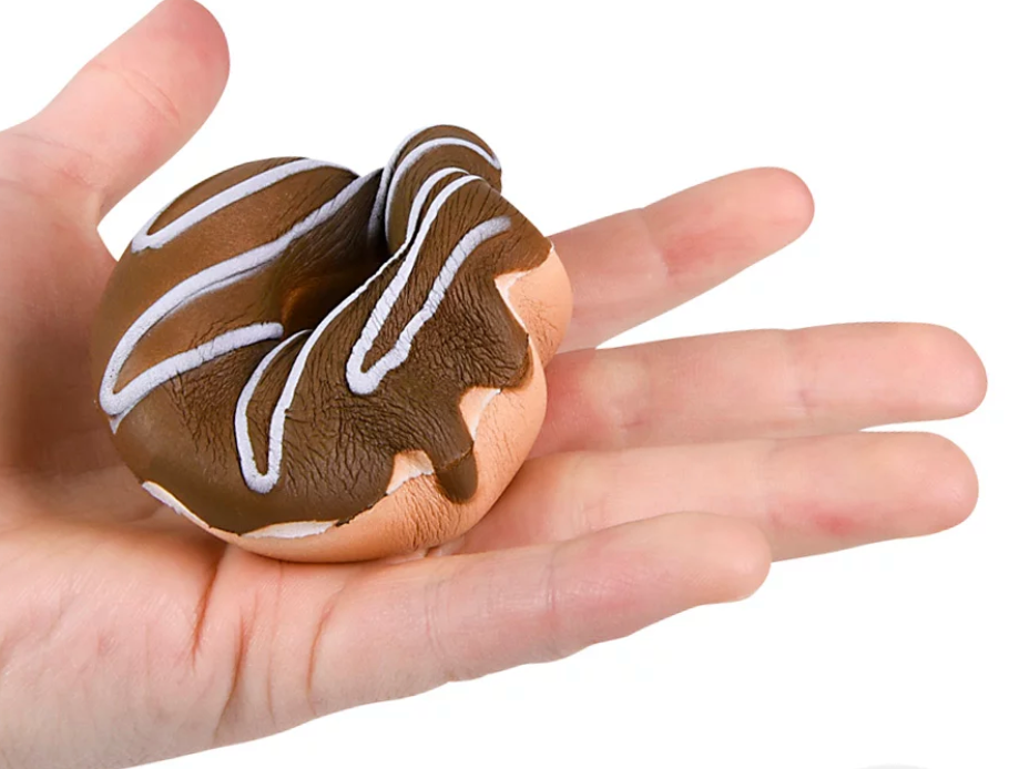 Hand holding a 3-inch Squishy Donut with chocolate frosting and white drizzle, soft and slow rising for stress relief.