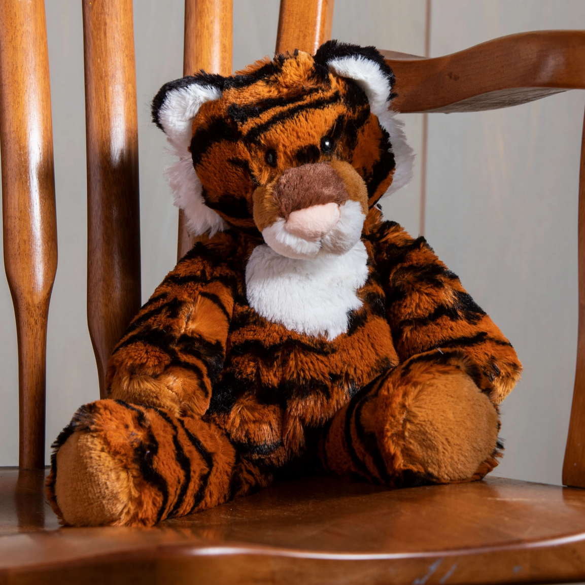Marshmallow Tiger plush toy sitting on a wooden chair, soft fabric with embroidered details and durable plastic eyes.