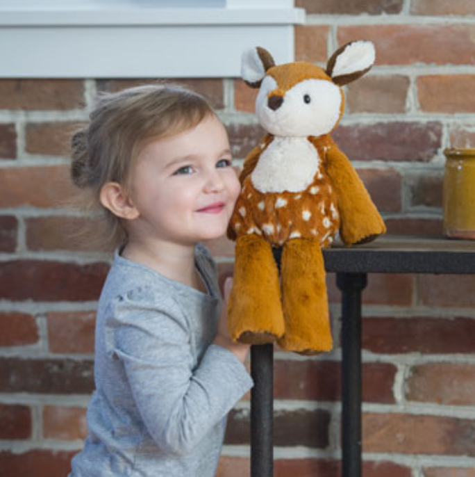 Child smiling and holding a soft plush Marshmallow Fawn toy with embroidered details and plastic eyes.