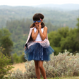Young girl wearing the Super Duper Tutu, Cape & Mask set in pink and navy standing outdoors with greenery background.
