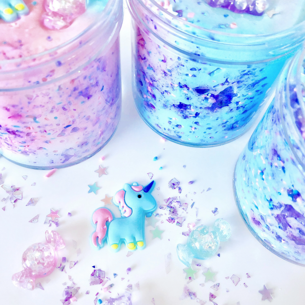 Close-up of colorful Don't Feed the Unicorns Butter Slime with unicorn charm and holographic stars in jars.