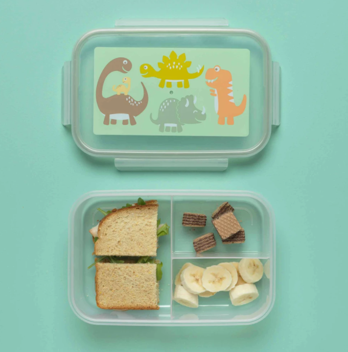 Good Lunch Bento Box | Baby Dinosaur with three compartments holding sandwich, banana slices, and snacks on blue background.