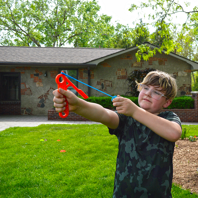 Child aiming and pulling back the Koosh Flingshot outdoors, ready to launch the special Koosh ball for fun play.