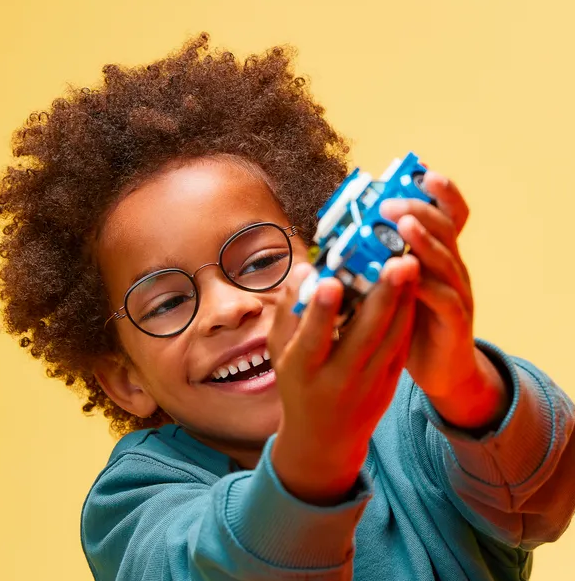 City Police Car toy held by a smiling child playing with a blue police patrol car LEGO set.