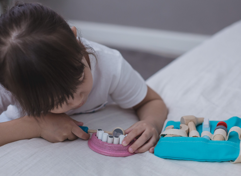 Child playing with wooden Dentist Set tools and teeth holder, practicing dental hygiene with pretend play kit.