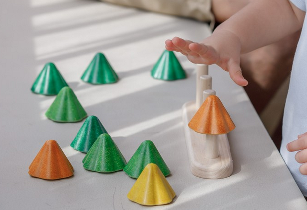 Child stacking colorful wooden pieces on rods in the Sort & Count Tree toy for counting and sorting practice.