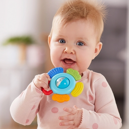 Baby holding a colorful Blossom Rattle & Teething Toy with spinning ball and textured teething elements.