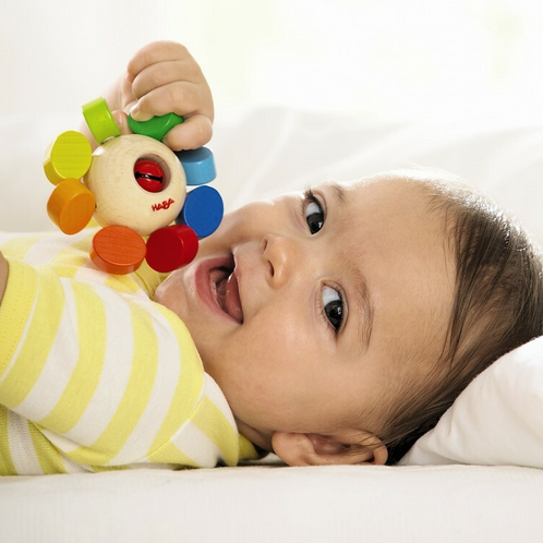 Baby playing with colorful wooden Clutching WhirlyGig toy designed to develop grasping skills and entertain infants.