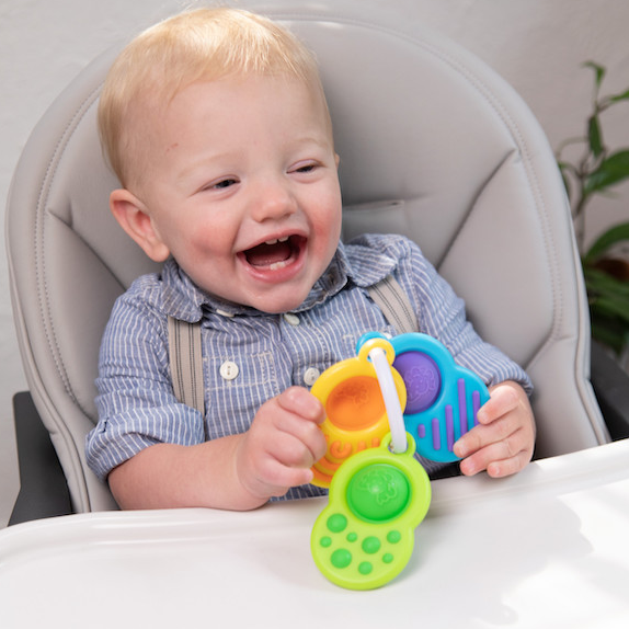 Happy toddler holding colorful Dimpl Clutch with sensory dimpl bubbles and silicone textures on clip ring.