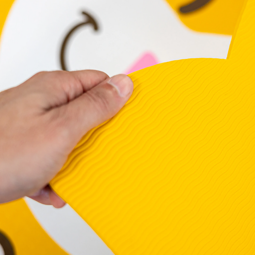Close-up of hand holding bright yellow Yoga Mat - Cat with textured surface and playful cat design for kids.