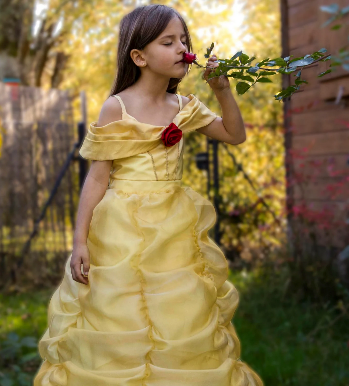 Girl in a garden wearing Belle Boutique Gown Size 5-6 smelling a red rose, pale yellow princess dress with hoop skirt.
