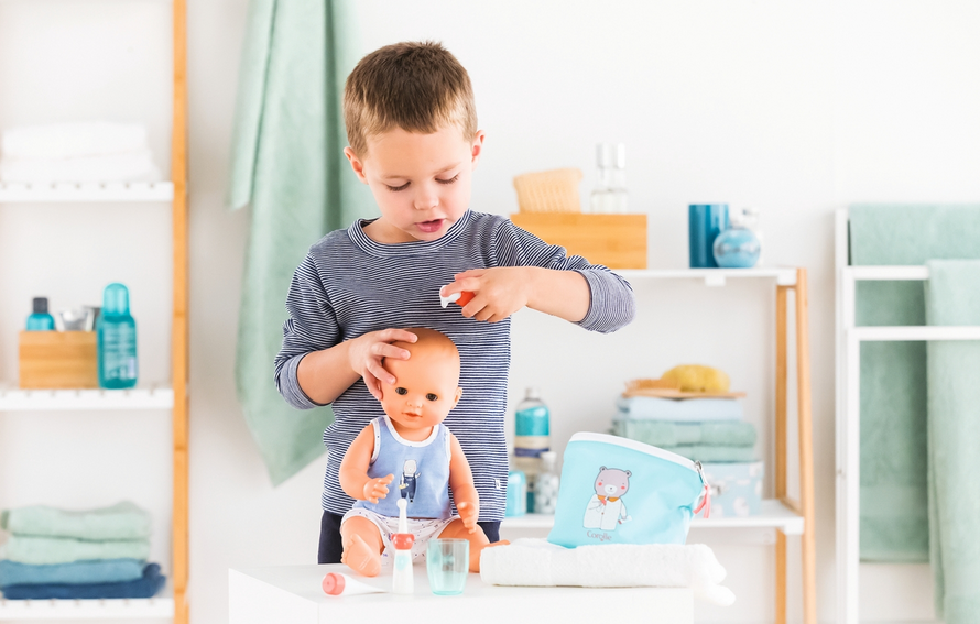 Young boy playing with Care Pouch & Accessories set, grooming a baby doll with lotion and toothbrush in a bright room.