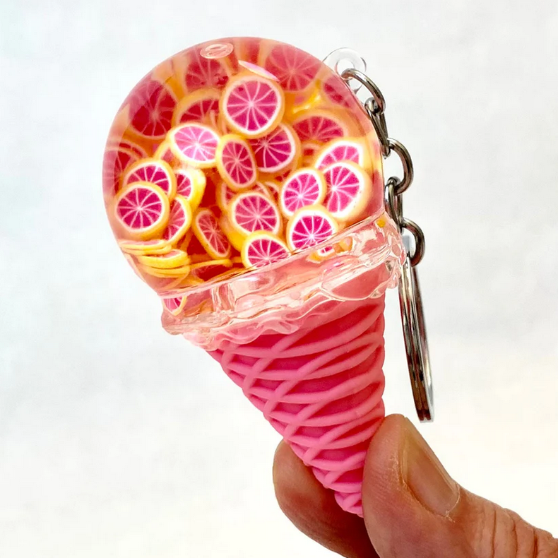Hand holding a pink cone Fruit Icecream Keychain decorated with realistic orange slice ice cream scoop and attached key ring.