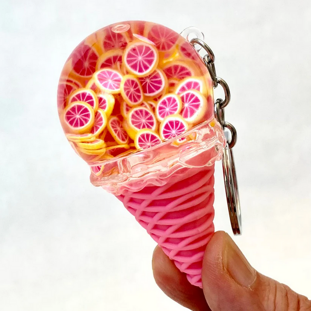 Hand holding a pink cone Fruit Icecream Keychain decorated with realistic orange slice ice cream scoop and attached key ring.