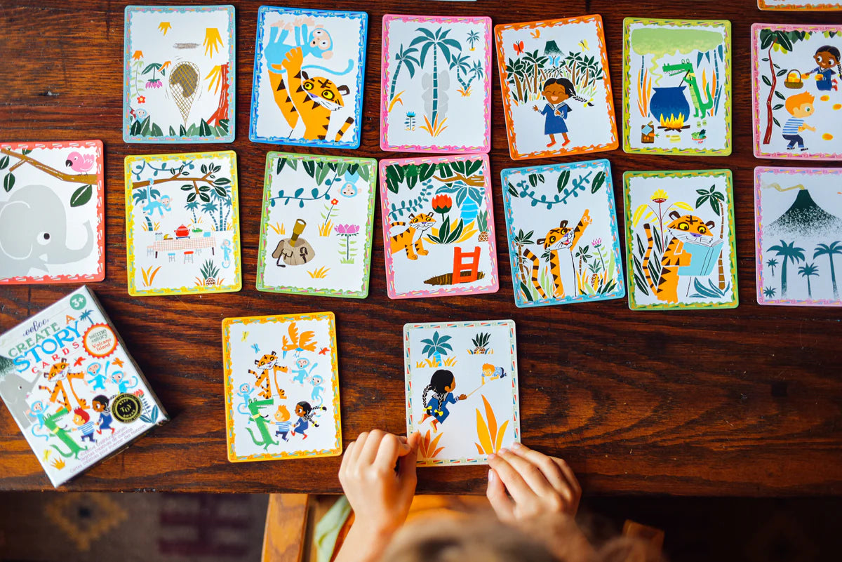 Create A Story | Volcano Island showing colorful illustrated story cards spread on a wooden table with child’s hands arranging them.