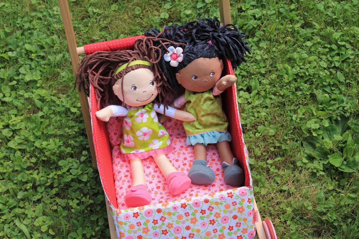 Soft Doll | Cari sitting in a floral stroller with another soft doll, both wearing colorful outfits outdoors.