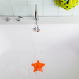 STAR Drain Cover in bright orange soaking in a white bathtub under running water with green bath toys nearby.