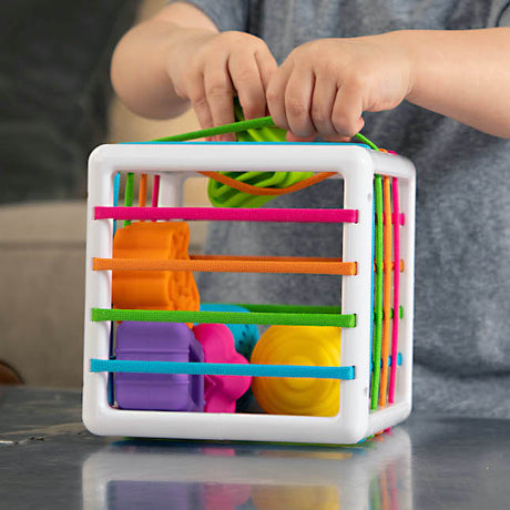 Child playing with colorful textured shapes in the Inny Bin shape-sorting cube toy for fine motor skills.