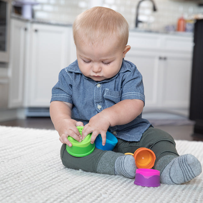 Baby playing with colorful stackable cups featuring textured silicone bubbles in the Dimpl Stack set.