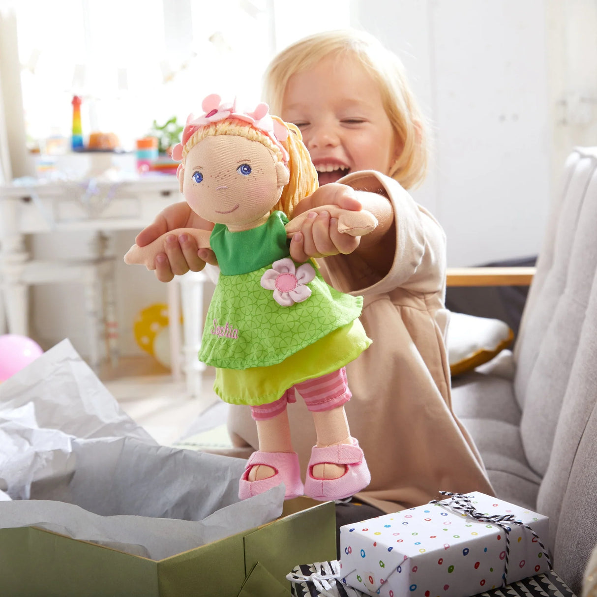 Soft Doll | Mali held by smiling child wearing a floral headband and green dress with pink shoes in bright room
