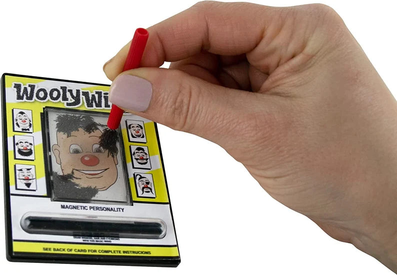 Hand holding magnetic wand drawing on the World’s Smallest Wooly Willy toy with silly clown faces around the board.