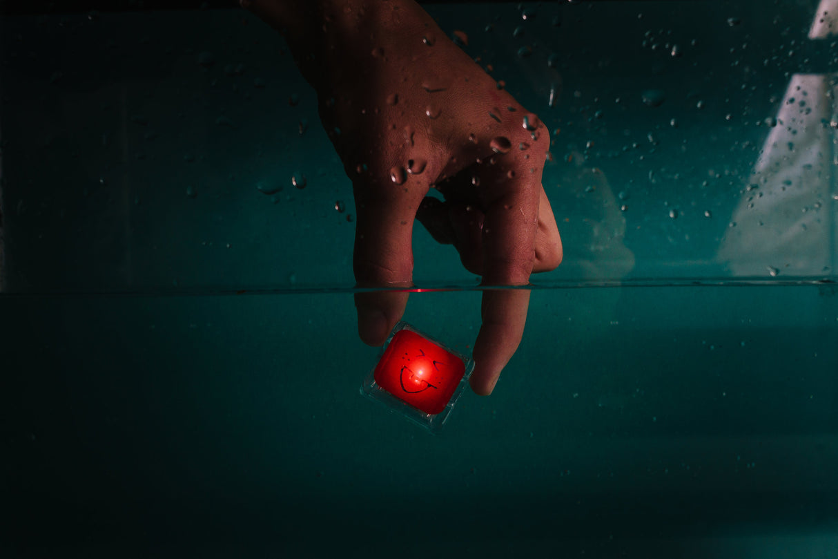 Hand placing a glowing red cube with a smiley face underwater, showcasing Glo Pals Red light-up toy.