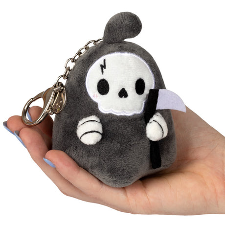 Hand holding a small plush keychain Reaper Micro with scythe and metal clip, soft polyester fiber design.