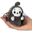 Hand holding a small plush keychain Reaper Micro with scythe and metal clip, soft polyester fiber design.