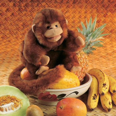 Monkey Puppet sitting among tropical fruits including bananas, pineapple, and melon on a woven mat background.