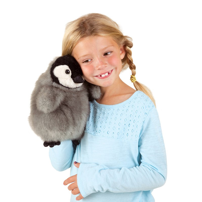 Young girl holding and smiling at the Emperor Penguin Baby Puppet with movable head and wings.